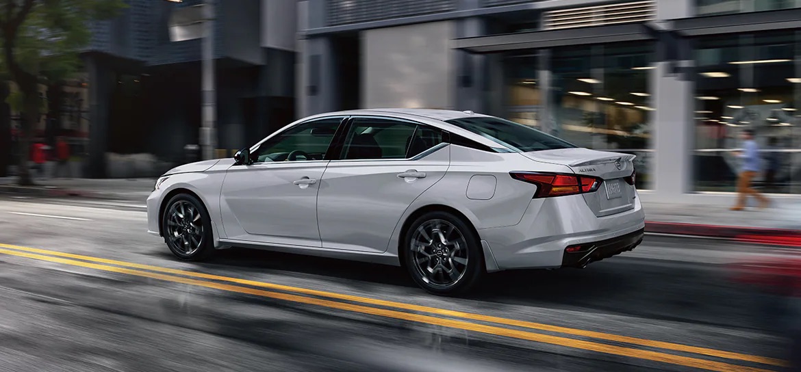 Silver 2024 Nissan Altima sedan driving down a city street during the rain